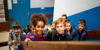 Mehrere Grundschulkinder laufen eine Treppe im Schulgebäude hoch.