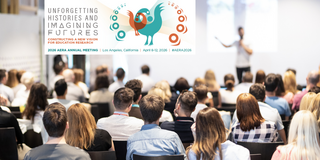 Konferenz Eine Gruppe von Menschen sitzt in einem großen Konferenzraum und hört einem Sprecher im Hintergrund zu