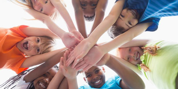 Grundschulkinder stehen im Kreis und halten ihre Hände zusammen