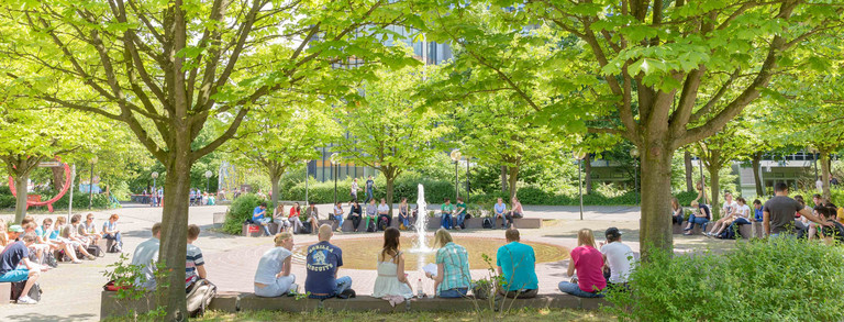 Studierende sitzend am Springbrunnen auf dem Campus Nord im Sommer