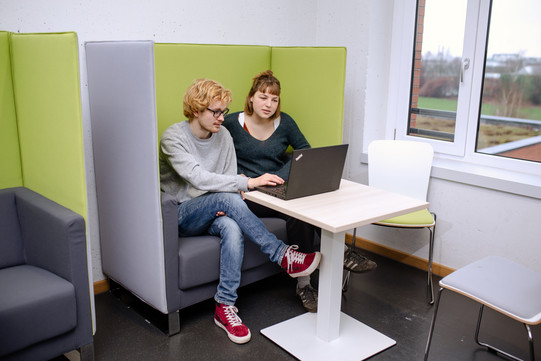 Zwei Studierende sitzen auf einem Sessel und sehen auf einen Laptop vor ihnen.