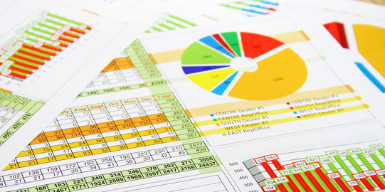 Paper pages with tables, pie charts, column charts as well as graph charts lie on top of each other.